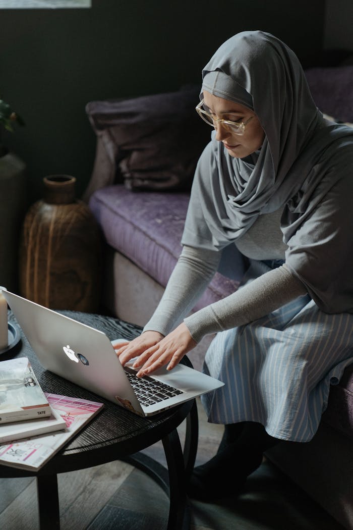Middle Eastern woman in hijab working on a laptop at home, focused and engaged.